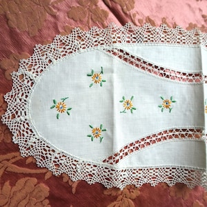Puede incluir: Un camino de mesa blanco de ganchillo con un borde festoneado y flores amarillas bordadas con hojas verdes.