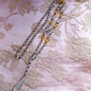 Peut inclure: Un long collier d&eacute;licat compos&eacute; de perles de verre transparentes et ambr&eacute;es. Le collier a un pendentif en forme de larme &agrave; l'extr&eacute;mit&eacute;.