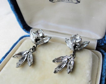 Peut inclure: Une paire de boucles d'oreilles pendantes en argent avec des pierres de cristal claires. Les boucles d'oreilles sont dans une boîte en velours avec le texte "S.H. LIMITED" à l'intérieur.