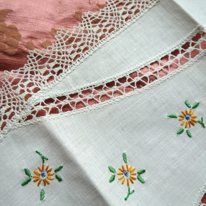 Puede incluir: Servilletas de lino blanco con flores amarillas bordadas y hojas verdes. Las servilletas tienen un delicado borde de encaje.