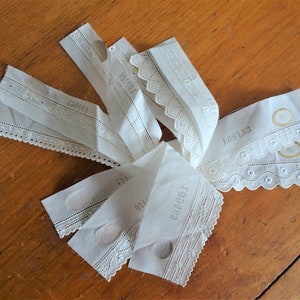 May include: A collection of white lace trim with different patterns and numbers printed on them. The trim is made of delicate fabric with a scalloped edge.