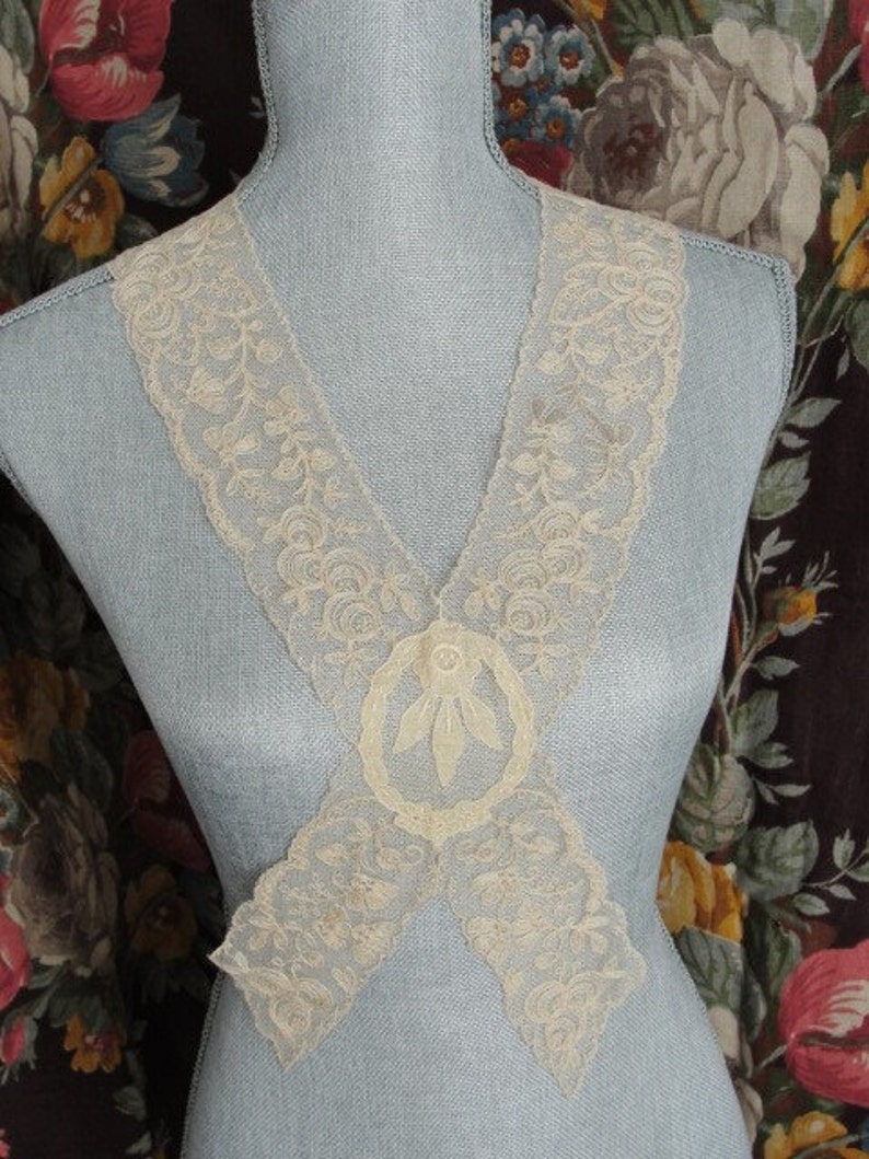 May include: A delicate white lace collar with a floral design. The collar is made of a fine, sheer fabric and has a delicate, feminine look.
