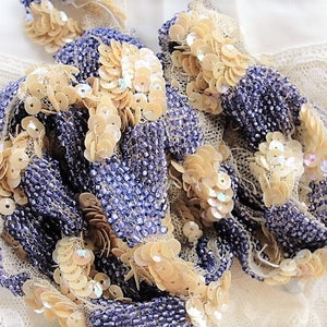 May include: A close-up of a beaded trim with iridescent sequins. The trim is made of small, purple beads and larger, iridescent sequins. The sequins are arranged in a pattern of rows and clusters.