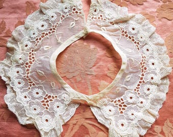 Puede incluir: Un cuello de encaje blanco con un borde festoneado y un delicado bordado floral. El cuello está hecho de una tela transparente y tiene un aspecto vintage.