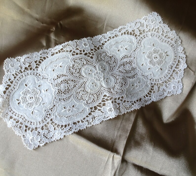Puede incluir: Un delicado tapete de encaje blanco con un dise&ntilde;o floral. El tapete presenta intrincados patrones de flores y calados, creando una apariencia texturizada y elegante. El encaje se coloca sobre un fondo neutro, resaltando sus intrincados detalles.