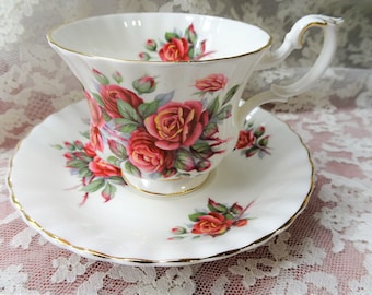 May include: A white teacup and saucer with a gold rim and a floral pattern of red roses and green leaves.