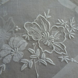 May include: White embroidered floral design on a sheer white fabric. The design features delicate flowers and leaves.
