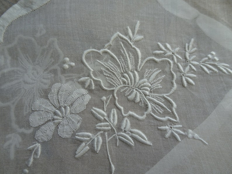 May include: White embroidered floral design on a sheer white fabric. The design features delicate flowers and leaves.