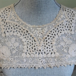 Puede incluir: Un delicado cuello de encaje blanco con borde festoneado. El cuello est&aacute; hecho de intrincado trabajo de ganchillo y presenta un dise&ntilde;o floral.