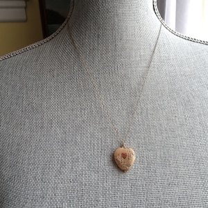 Op de afbeelding: Een gouden ketting met een hartvormige hanger aan een delicate ketting. De hanger heeft een bloemmotief en een klein hartje in het midden.