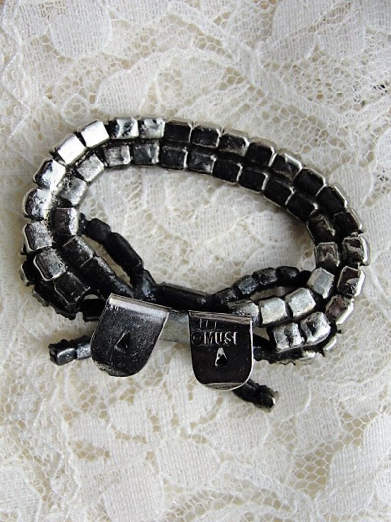 K&ouml;nnte beinhalten: Ein silbernes und schwarzes Armband mit einer doppelten Reihe quadratischer Perlen. Das Armband hat einen Verschluss mit der Gravur "OMUST".