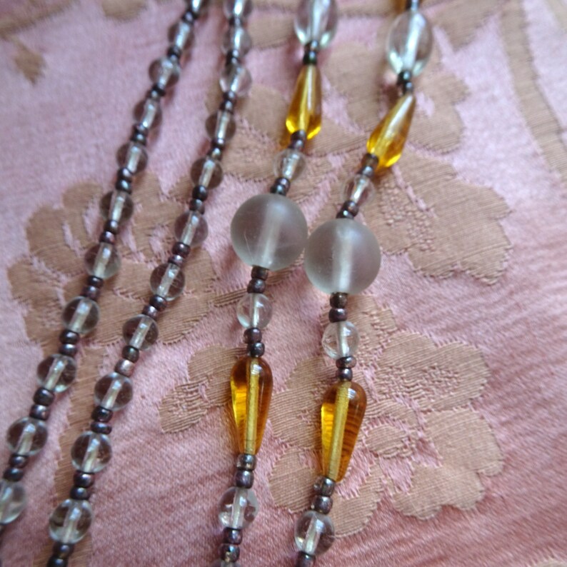 Peut inclure: Un collier multi-rangs avec des perles de verre transparentes et des perles en forme de larme de couleur ambre.
