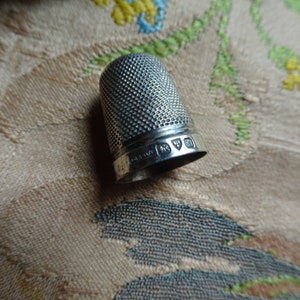 May include: Silver thimble with a textured surface and hallmarks on the band. The hallmarks include a lion, a crown, and a letter.