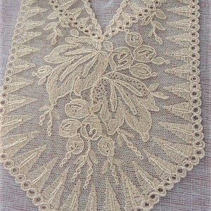 May include: A delicate, off-white lace collar with a floral design. The lace is intricate and features a scalloped edge.