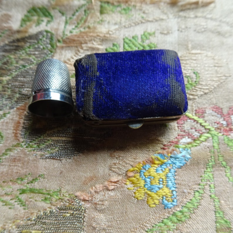 May include: A silver thimble with a blue velvet sewing box. The box has a metal clasp.