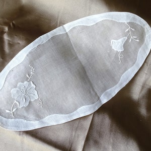 May include: White oval-shaped linen table runner with embroidered floral designs. The runner has a scalloped edge.
