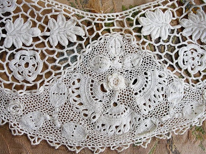 May include: White crocheted lace trim with a delicate floral pattern. The lace is made with a fine thread and has a scalloped edge.