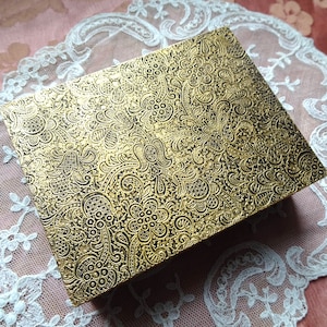 May include: A gold box with a black and gold paisley pattern. The box is made of a textured material and has a slightly raised design.