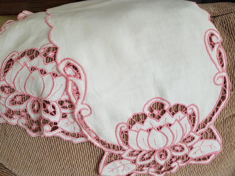 May include: White linen table runner with pink embroidered floral design. The design features delicate flowers and leaves.