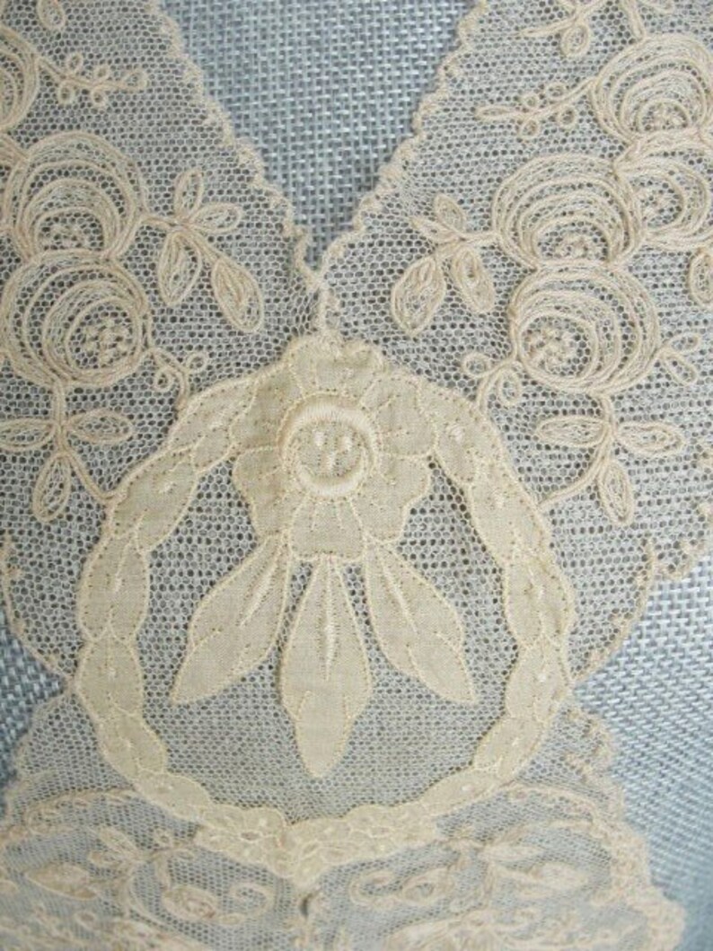 May include: Close-up of a delicate white lace fabric with a floral design. The lace features intricate details, including small flowers and leaves.