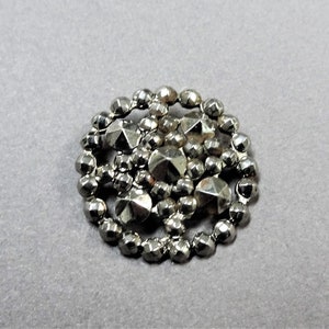 May include: A silver button with a round shape and a raised design of small, faceted beads.