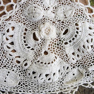 May include: White crocheted lace doily with a delicate floral design. The lace is intricate and detailed, with a variety of stitches and patterns.