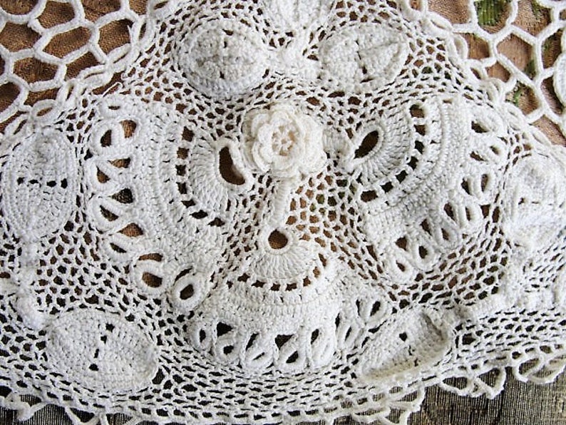 May include: White crocheted lace doily with a delicate floral design. The lace is intricate and detailed, with a variety of stitches and patterns.