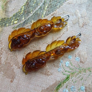 Peut inclure: Deux pinces à cheveux en verre ambré en forme de feuilles avec une pince en métal argenté à chaque extrémité.