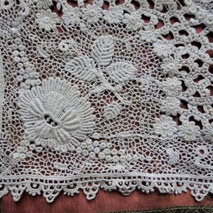 Puede incluir: Un encaje de ganchillo blanco con un delicado patr&oacute;n floral. El encaje es intrincado y detallado, con un borde festoneado.