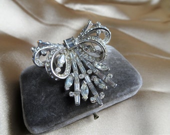 Peut inclure: Une broche en argent avec un grand nœud et une cascade de strass transparents.