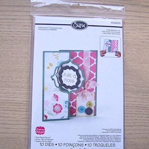 May include: A clear plastic package containing a card-making die set. The card features floral and geometric patterns, with the words "Just a note" in a decorative frame. Includes 10 dies and 10 punches.