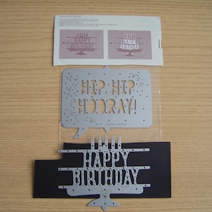 May include: A collection of silver metal die cuts for crafting. Includes a speech bubble with "HIP HIP HOORAY!" and a "HAPPY BIRTHDAY" cake design. Also includes a paper with instructions and a "HAPPY BIRTHDAY" cake design.