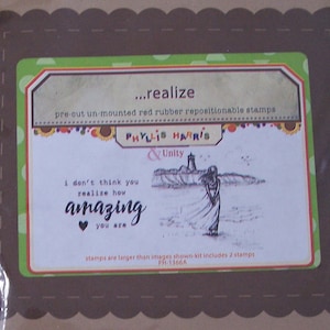 May include: A brown and green card with a scalloped border. The card features a pre-cut un-mounted red rubber repositionable stamp set by Phyllis Harris & Unity. The stamp set includes a lighthouse, a woman, and the text "I don't think you realize how amazing you are".