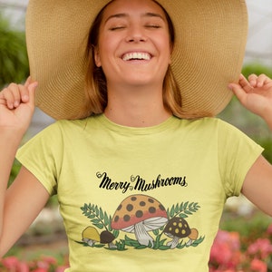 K&ouml;nnte beinhalten: Ein gelbes T-Shirt mit einem Aufdruck von Pilzen und dem Text "Merry Mushrooms".