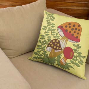Puede incluir: Una almohada amarilla con un dise&ntilde;o de setas. Las setas son rojas, naranjas, marrones y blancas con manchas marrones. Las hojas verdes rodean las setas.