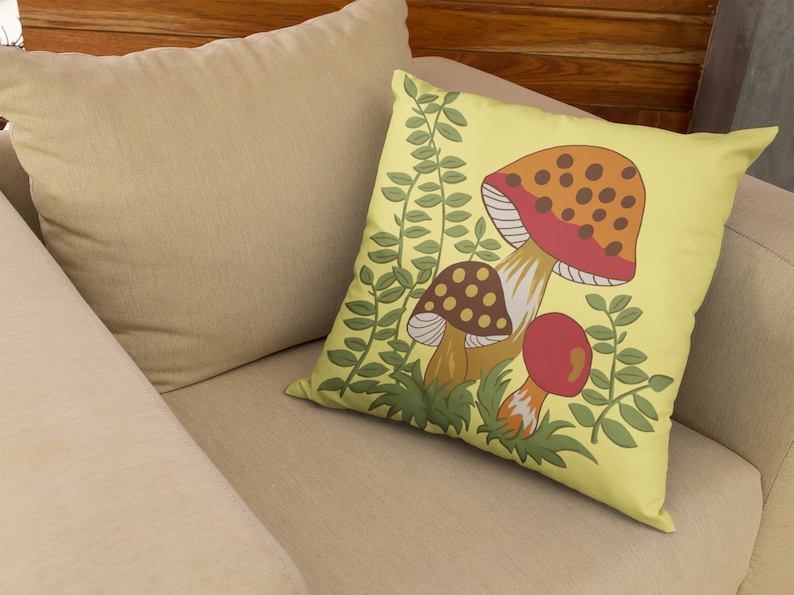 Puede incluir: Una almohada amarilla con un dise&ntilde;o de setas. Las setas son rojas, naranjas, marrones y blancas con manchas marrones. Las hojas verdes rodean las setas.