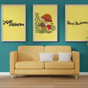 Puede incluir: Tres impresiones enmarcadas con fondo amarillo y texto negro que dice "Merry Mushrooms". La impresi&oacute;n central presenta una ilustraci&oacute;n de hongo con acentos rojos y marrones y hojas verdes. Las impresiones est&aacute;n colgadas en una pared azul verdosa sobre un sof&aacute; amarillo.