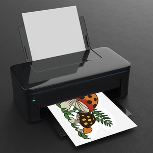 K&ouml;nnte beinhalten: Eine Schwarzwei&szlig;illustration von drei Pilzen mit orangefarbenen, roten und gelben Akzenten. Die Pilze sind von gr&uuml;nen Bl&auml;ttern umgeben. Die Illustration wird auf einem wei&szlig;en Blatt Papier von einem schwarzen Drucker gedruckt.