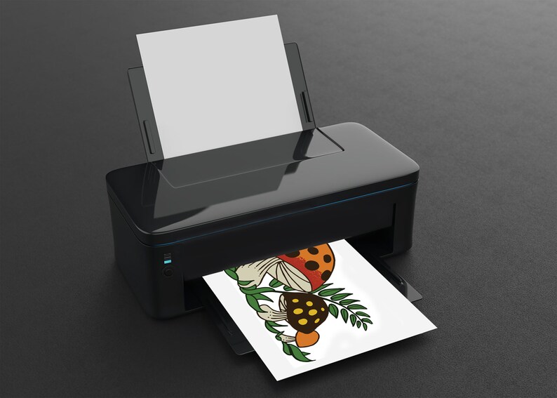 K&ouml;nnte beinhalten: Eine Schwarzwei&szlig;illustration von drei Pilzen mit orangefarbenen, roten und gelben Akzenten. Die Pilze sind von gr&uuml;nen Bl&auml;ttern umgeben. Die Illustration wird auf einem wei&szlig;en Blatt Papier von einem schwarzen Drucker gedruckt.
