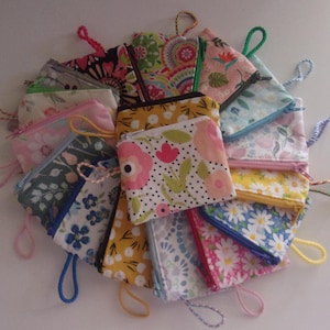 May include: A collection of small, colorful fabric zipper pouches with various floral and patterned designs. Each pouch has a matching zipper and a loop for carrying. The pouches are arranged in a circular pattern, showcasing a variety of colors and patterns.
