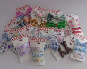 May include: A collection of colorful hair bows and hair clips on display. The bows feature various patterns, including floral, gingham, and solid colors. The hair clips are adorned with flowers and ribbons. Each item is attached to a white card with a red and white cherry design.