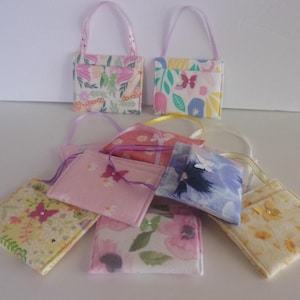 May include: A collection of small, fabric purses with floral and butterfly patterns. Two purses have ribbon handles, while the others have ribbon loops. The purses feature various colors, including pink, yellow, and blue, with a white background.