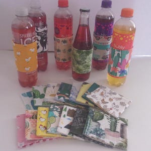 May include: A collection of fabric bottle sleeves featuring various colourful patterns including cacti, chickens, and mountain landscapes, displayed both wrapped around plastic and glass beverage bottles and folded in a stack in the foreground.