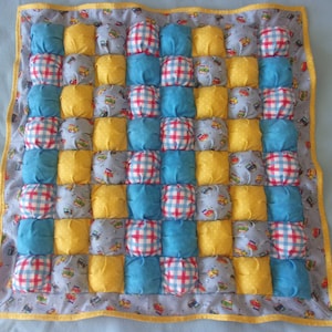 May include: A yellow, blue, and white quilted baby blanket with a checkered pattern. The blanket is made of soft, plush fabric and is perfect for cuddling.