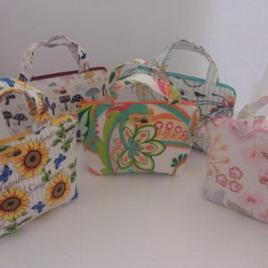 May include: Five small, colorful, fabric handbags with different patterns. The handbags have a top zipper closure and a fabric handle. The patterns include sunflowers, mushrooms, paisley, butterflies, and flowers.