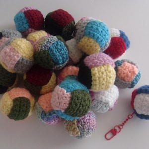 May include: A collection of colorful, crocheted balls in various sizes and colors, including blue, red, yellow, pink, and green. One ball has a red clasp attached. The balls are likely handmade and suitable for play or decoration.