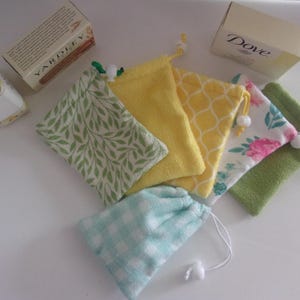 May include: Five small fabric bags with different patterns. The bags are yellow, green, blue, and white with floral and geometric designs. The bags are arranged on a white surface.  The bags are labeled "YARDLEY" and "Dove".