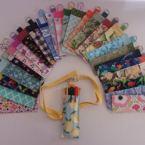 May include: A collection of colourful fabric pencil cases with keyrings, some with floral, geometric, and animal prints. A yellow lanyard with a blue and yellow lemon print pencil case is also included.