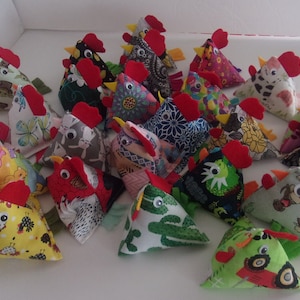 May include: A collection of colorful, handmade fabric chickens. Each chicken is a different pattern and has a red comb and wattle. The chickens are arranged in a pile on a white surface.