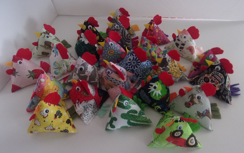May include: A collection of colorful, handmade fabric chickens. Each chicken is a different pattern and has a red comb and wattle. The chickens are arranged in a pile on a white surface.